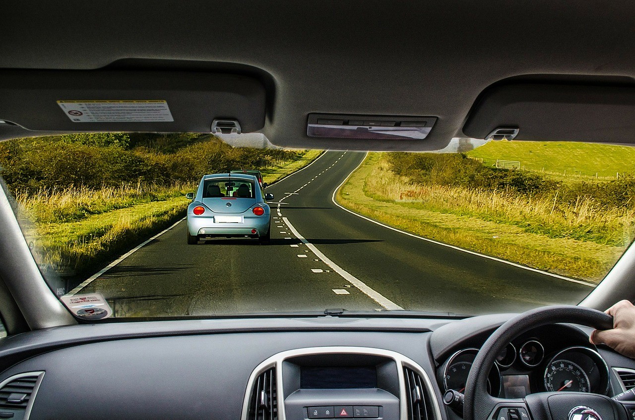 view out the windscreen of a car with 2 cars ahead on the road and grass either side of the road